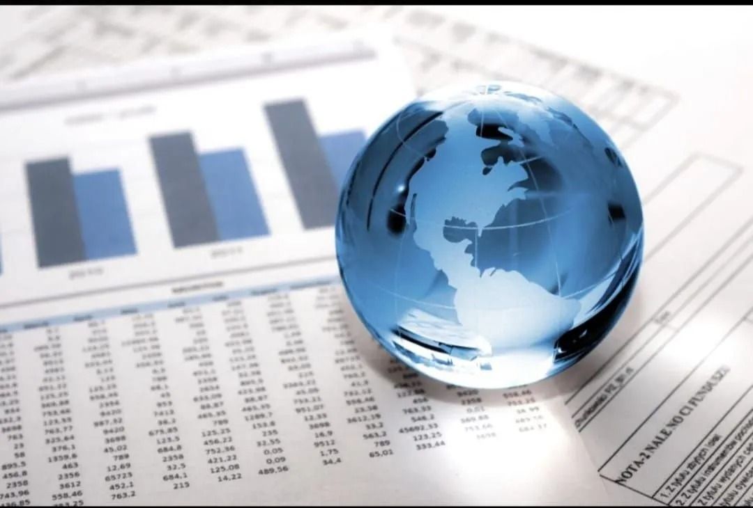 Un globo terráqueo de cristal azul descansa sobre una hoja con tablas de datos financieros y un gráfico de barras.