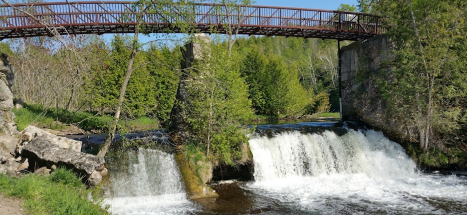 An old, iron bridge over a stream with a damn