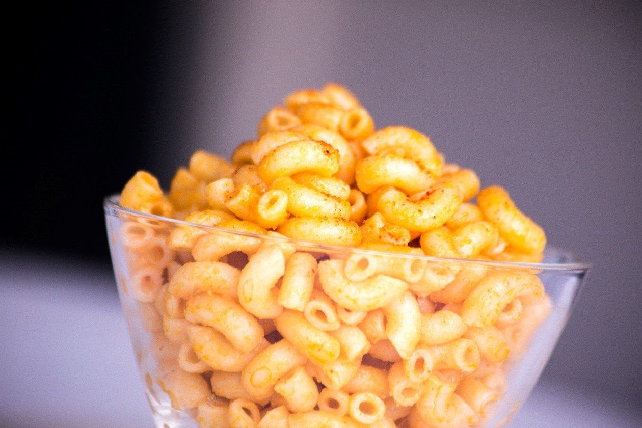 A clear bowl with cheesy macaroni pasta inside of it.