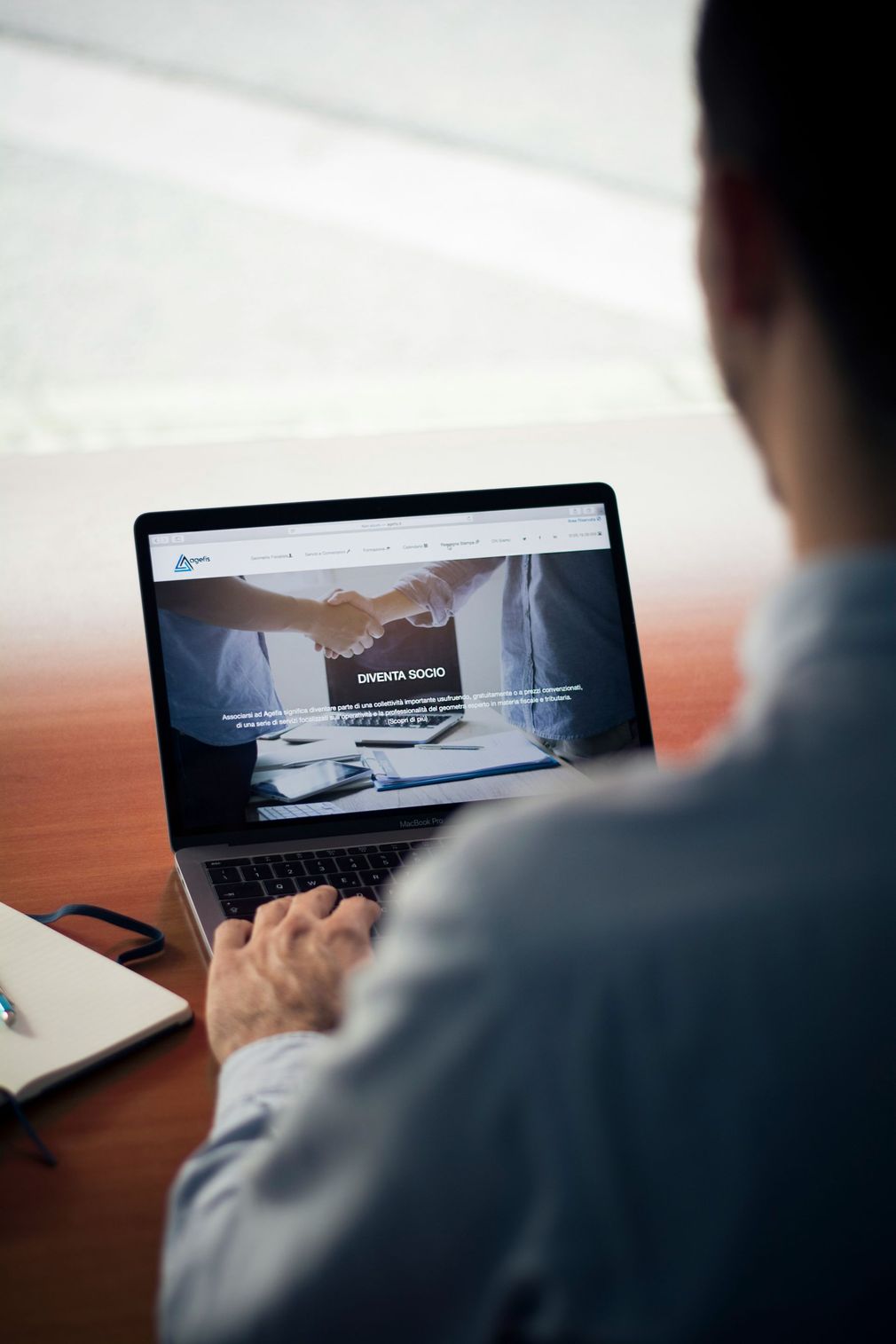 Person using a laptop at a desk, viewing a website with a mountain landscape on screen