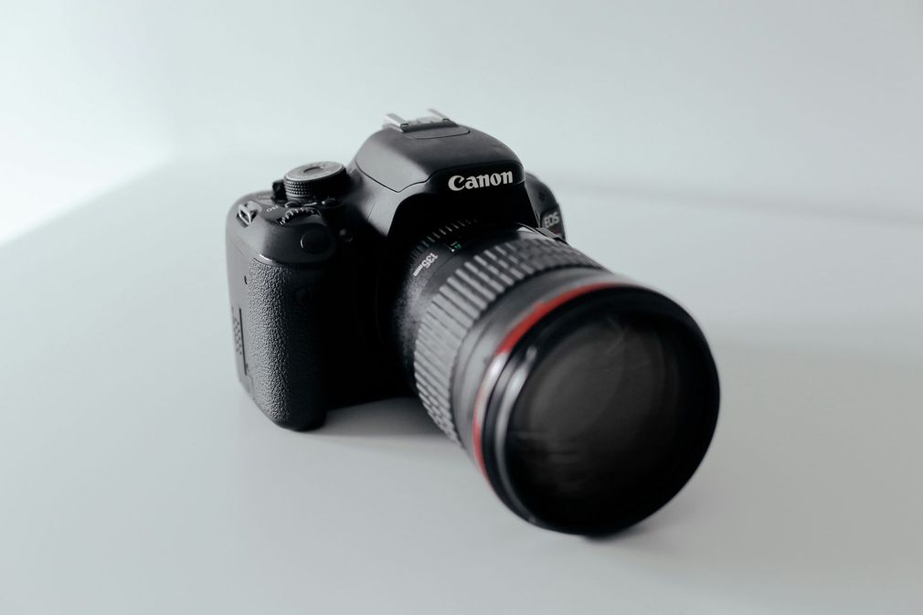 Black Canon DSLR camera with zoom lens on a light gray surface