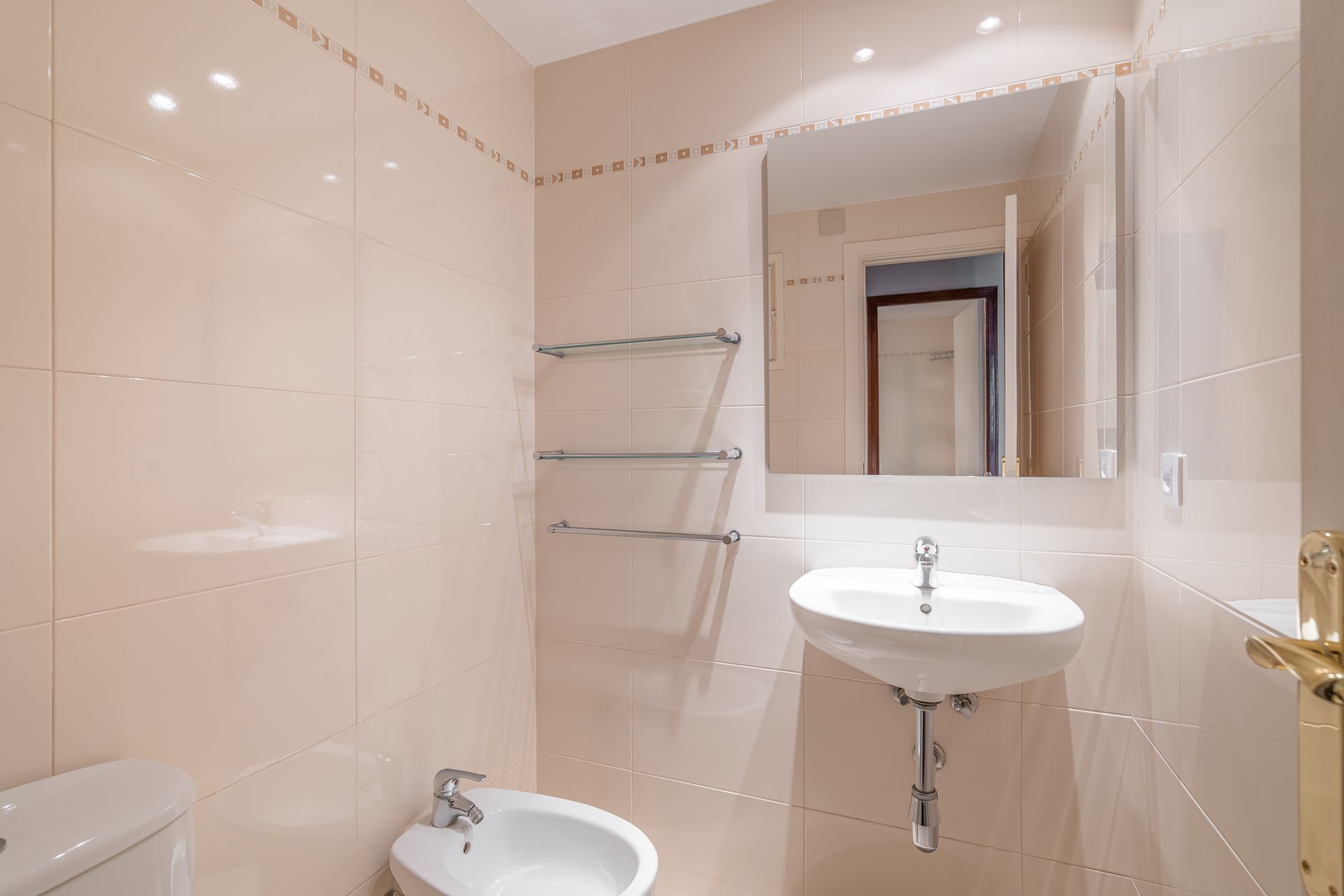 A small, beige-tiled bathroom with a sink, mirror, and bidet.