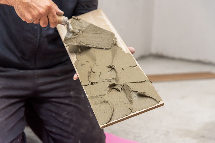 Person applies mortar to a tile with a trowel, indoors.