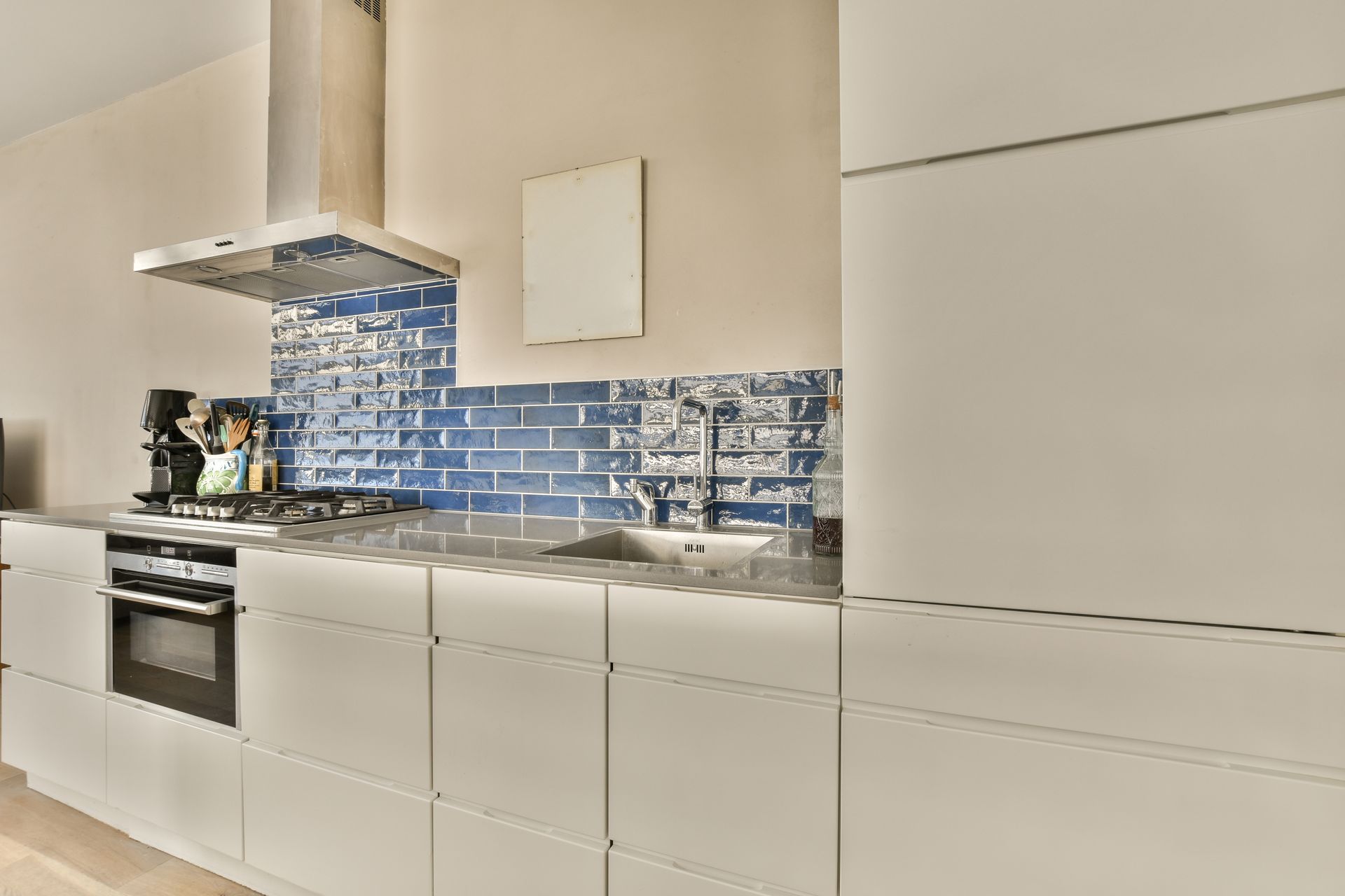 Modern kitchen with white cabinetry, blue backsplash, and stainless steel range hood.