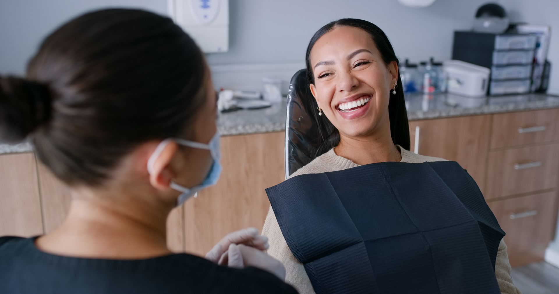 Woman with short, white hair smiles while in a dentist's chair; blue chair and bib.