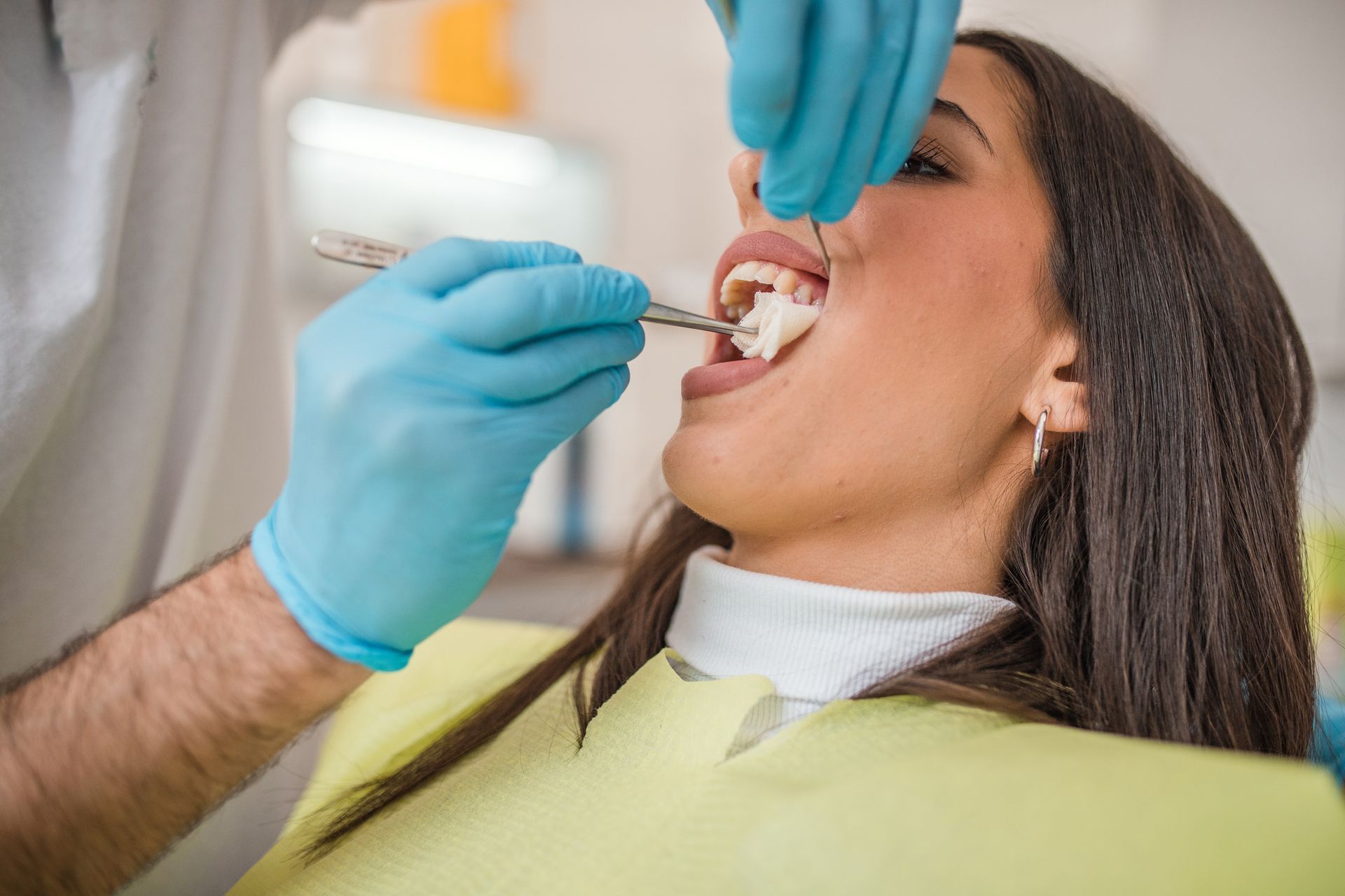 Dentist in pink scrubs pointing at a screen, explaining to a smiling patient in a dental chair.