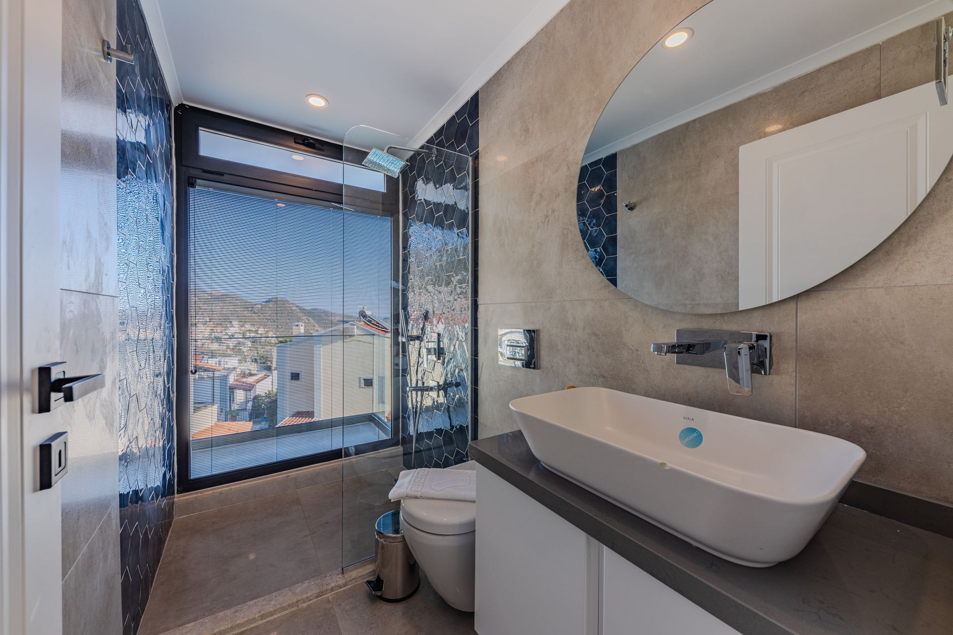 Modern bathroom with walk-in shower, round mirror, vessel sink, and large window with city view