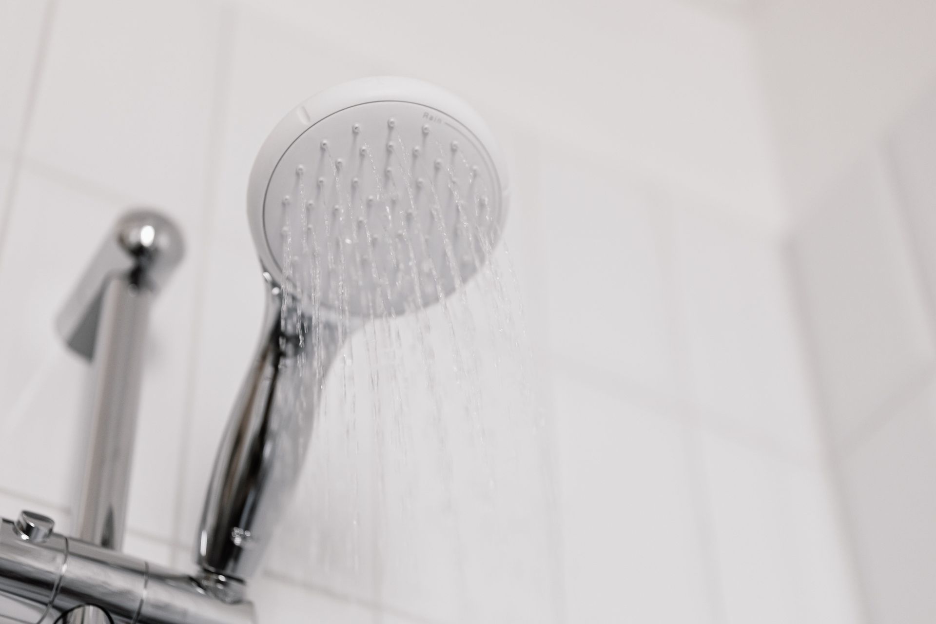 Chrome showerhead spraying water in a white tiled shower