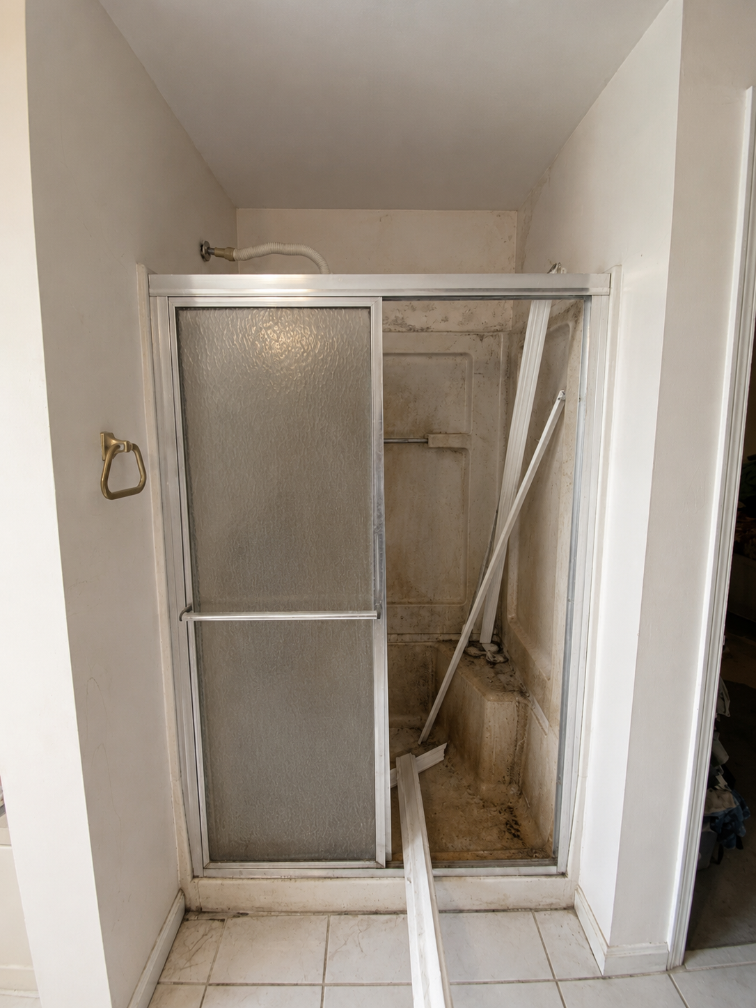 Broken shower enclosure with a shattered sliding door and detached panel in a bathroom.