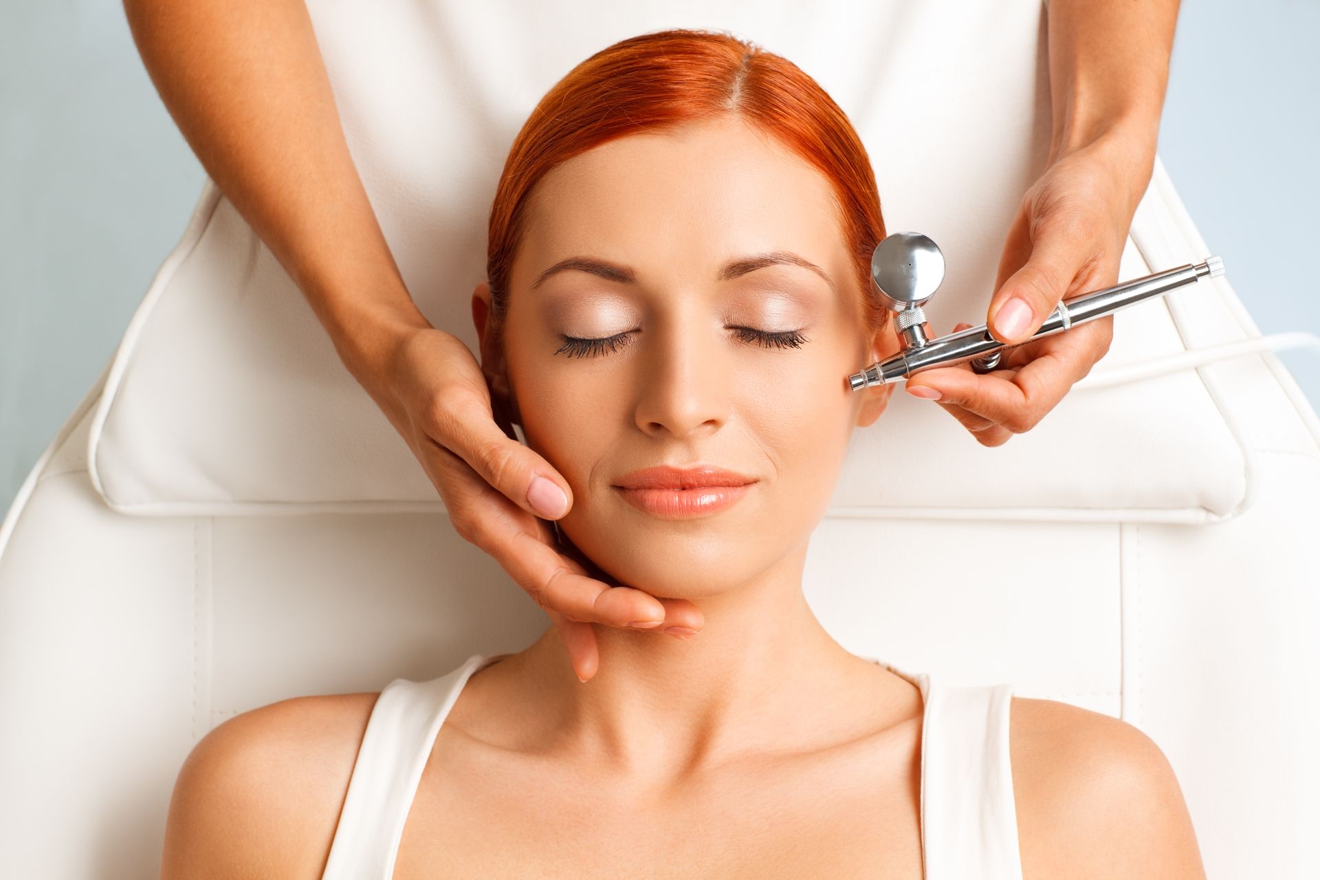 A woman is getting an airbrush treatment on her face.