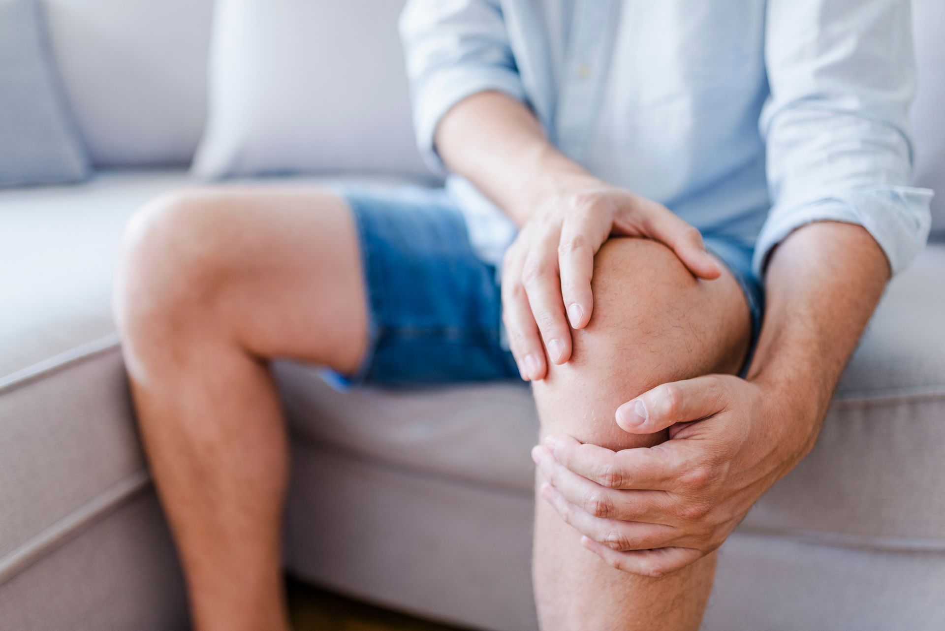 A man is sitting on a couch holding his knee in pain