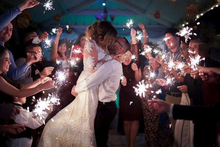 Newlyweds kiss amidst sparklers held by guests at a wedding reception.