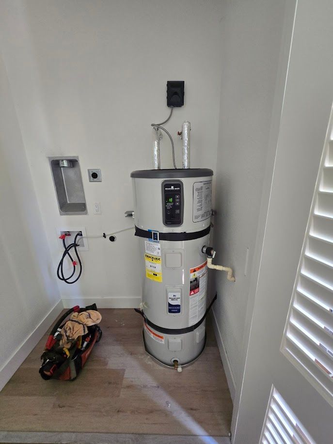 A water heater in a utility closet with washing machine hookups, and a toolbox on the floor.
