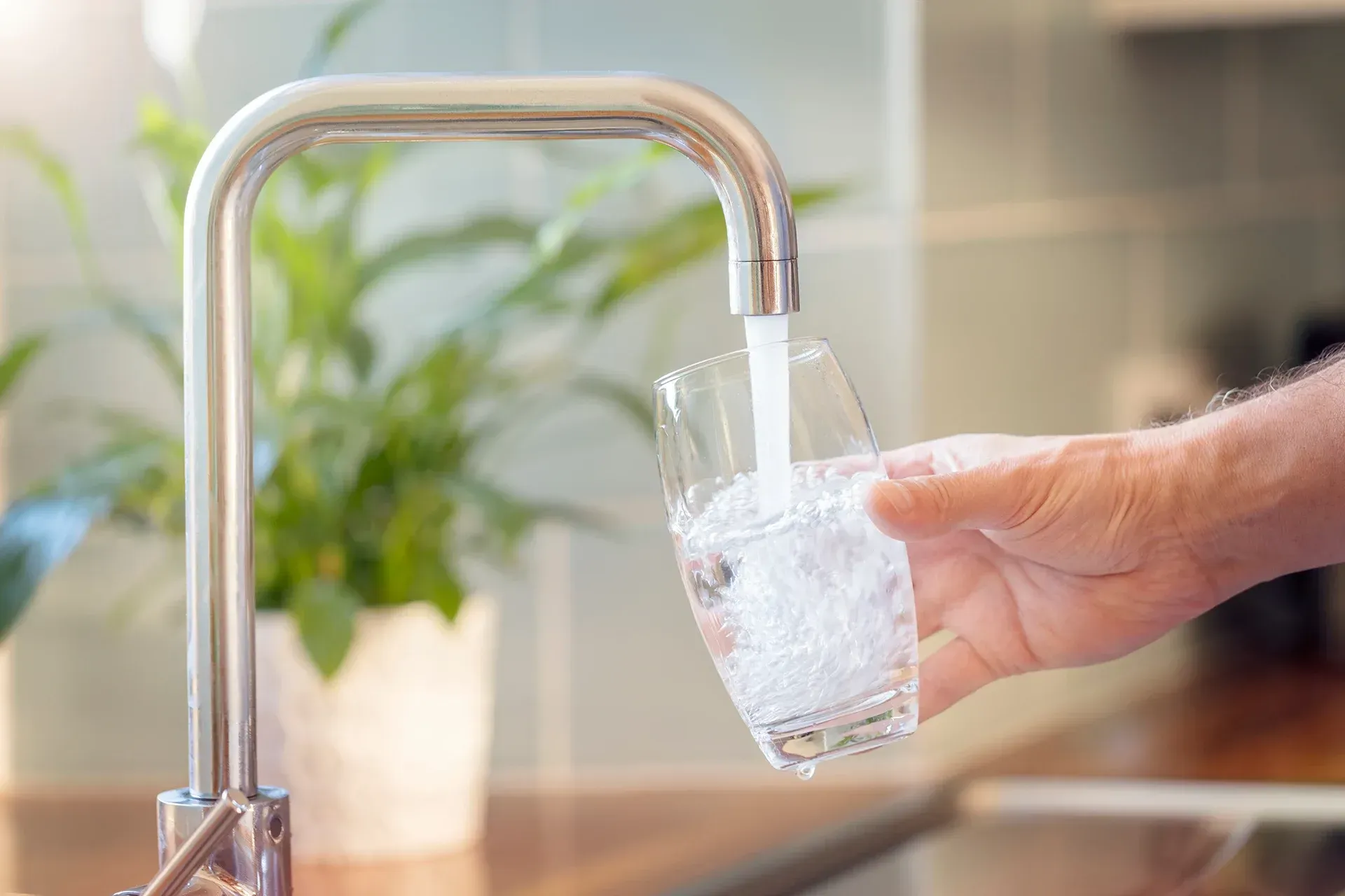 A person is pouring water into a glass from a faucet.