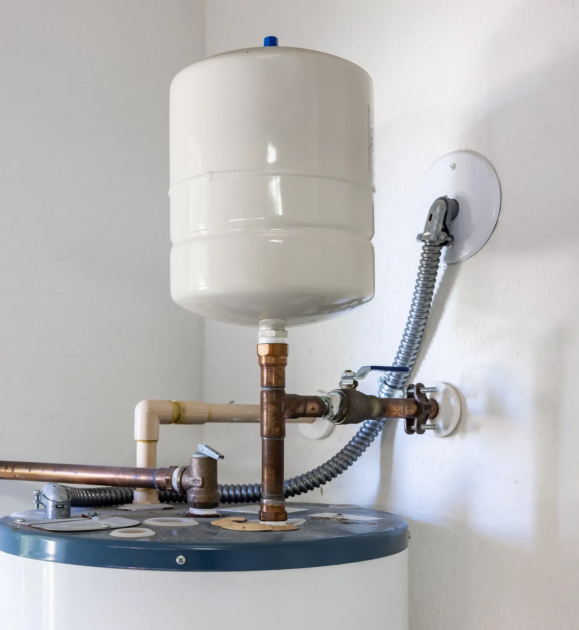 White water heater with expansion tank and copper pipes against a white wall.