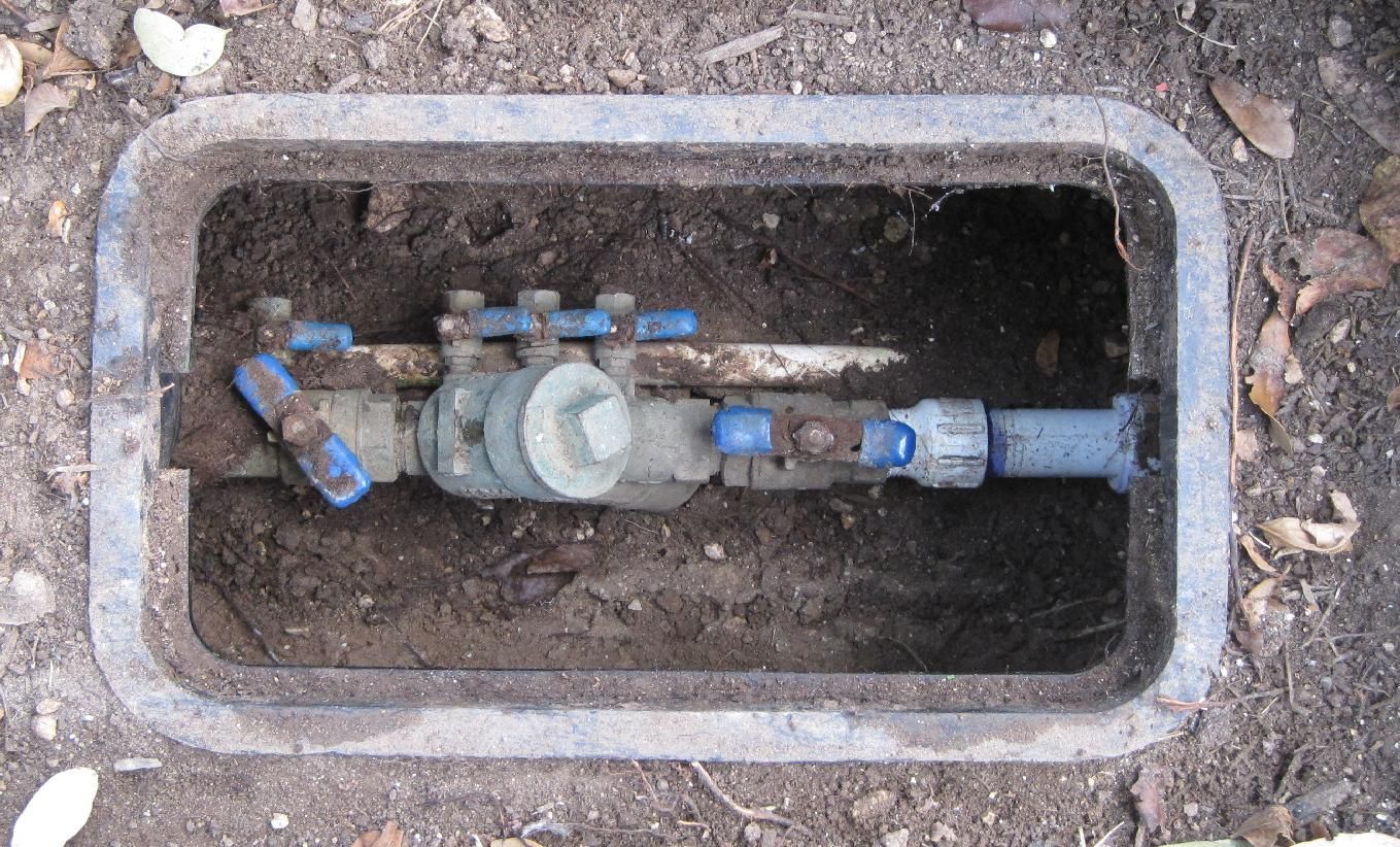 Water meter and valves inside a rectangular plastic access box in the ground.