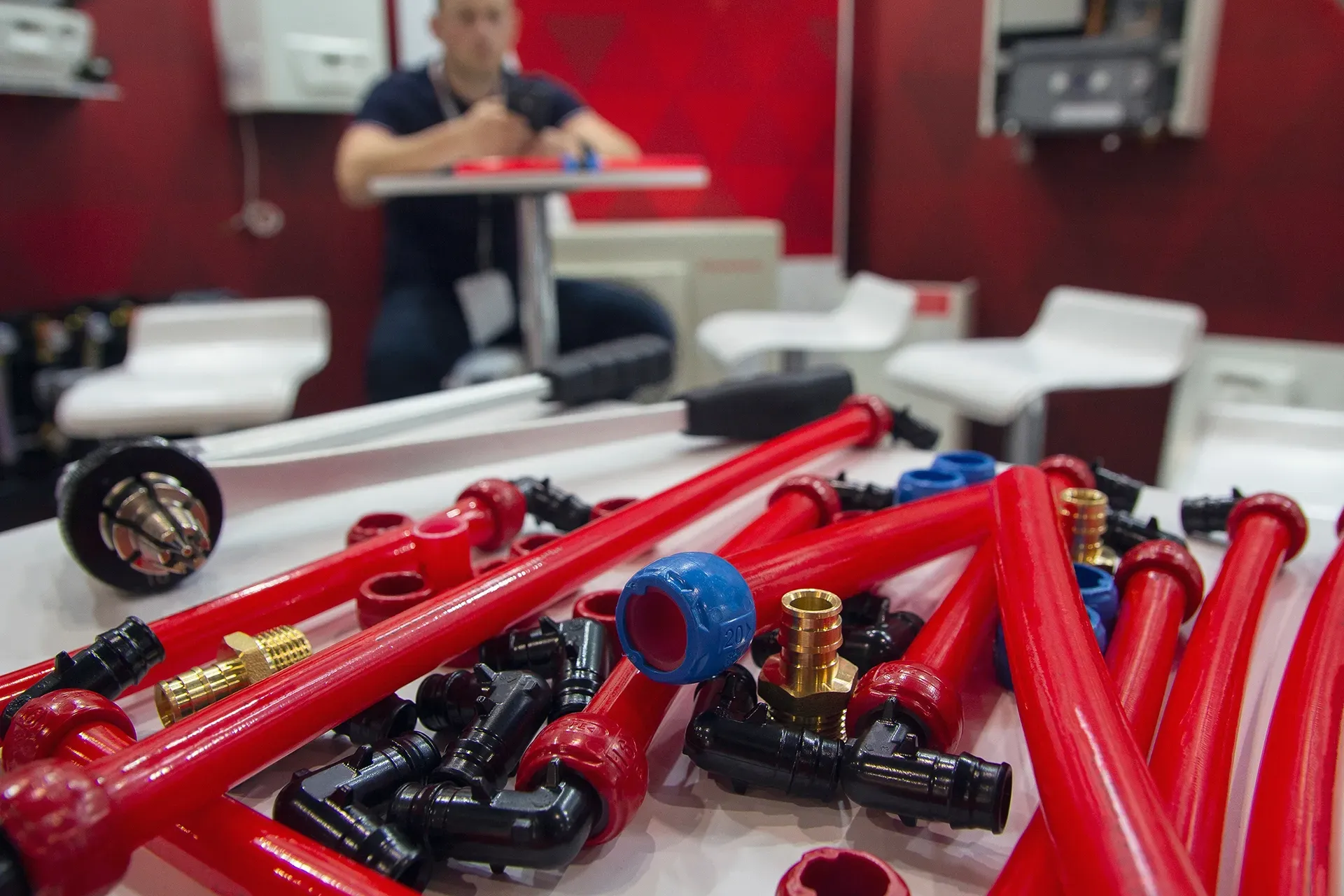 a bunch of red pipes and fittings on a table with a man sitting at a table in the background .