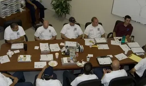 A group of men are sitting around a table with papers on it