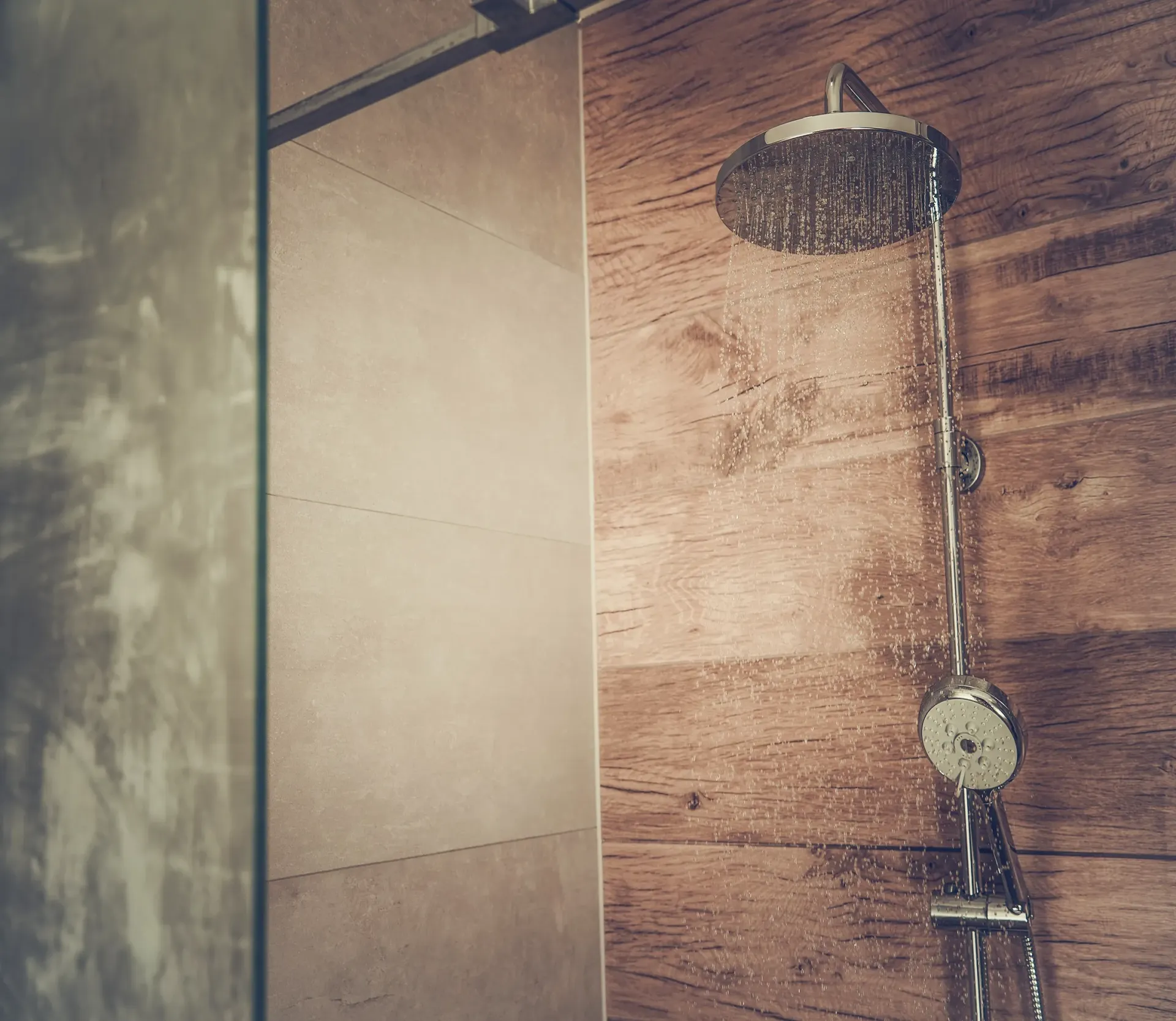 A shower head with hot water coming out hangs from a wooden wall in a bathroom.
