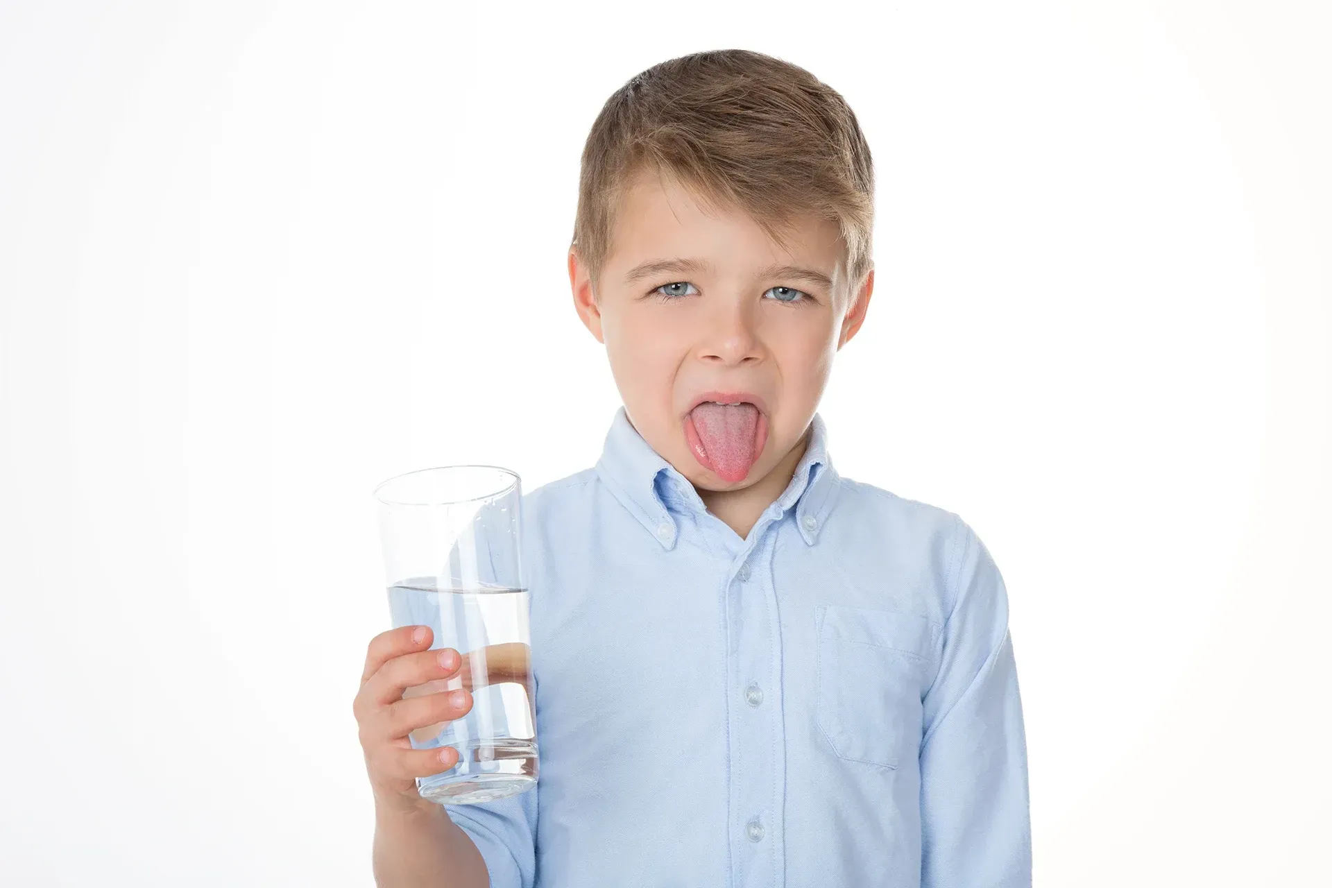 A young boy is sticking his tongue out while holding a glass of water.