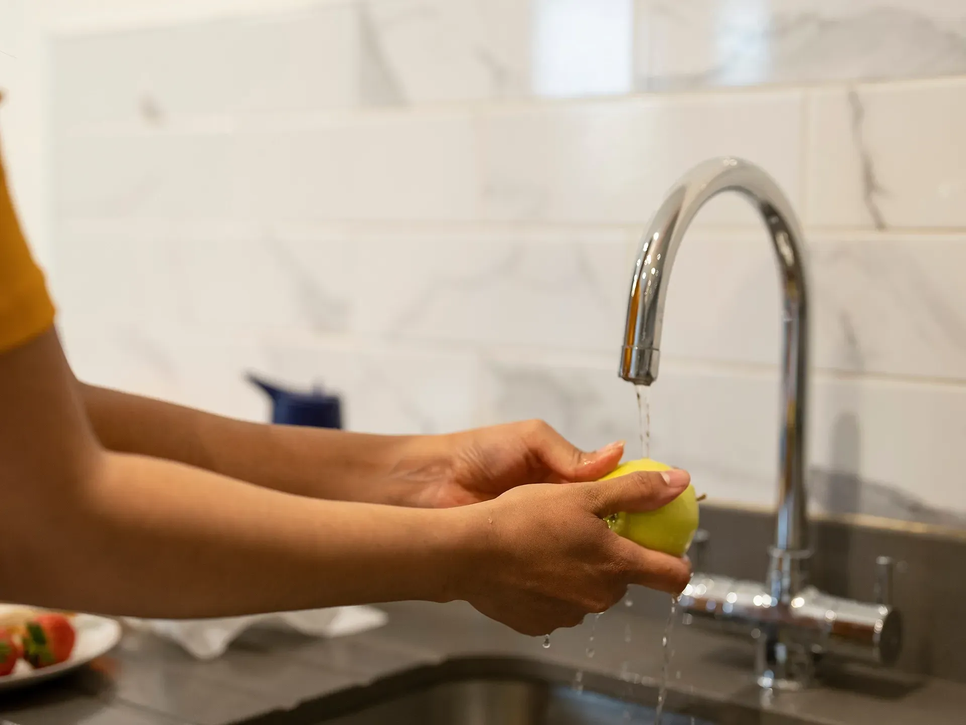 a person washing fruit at a kitchen sink