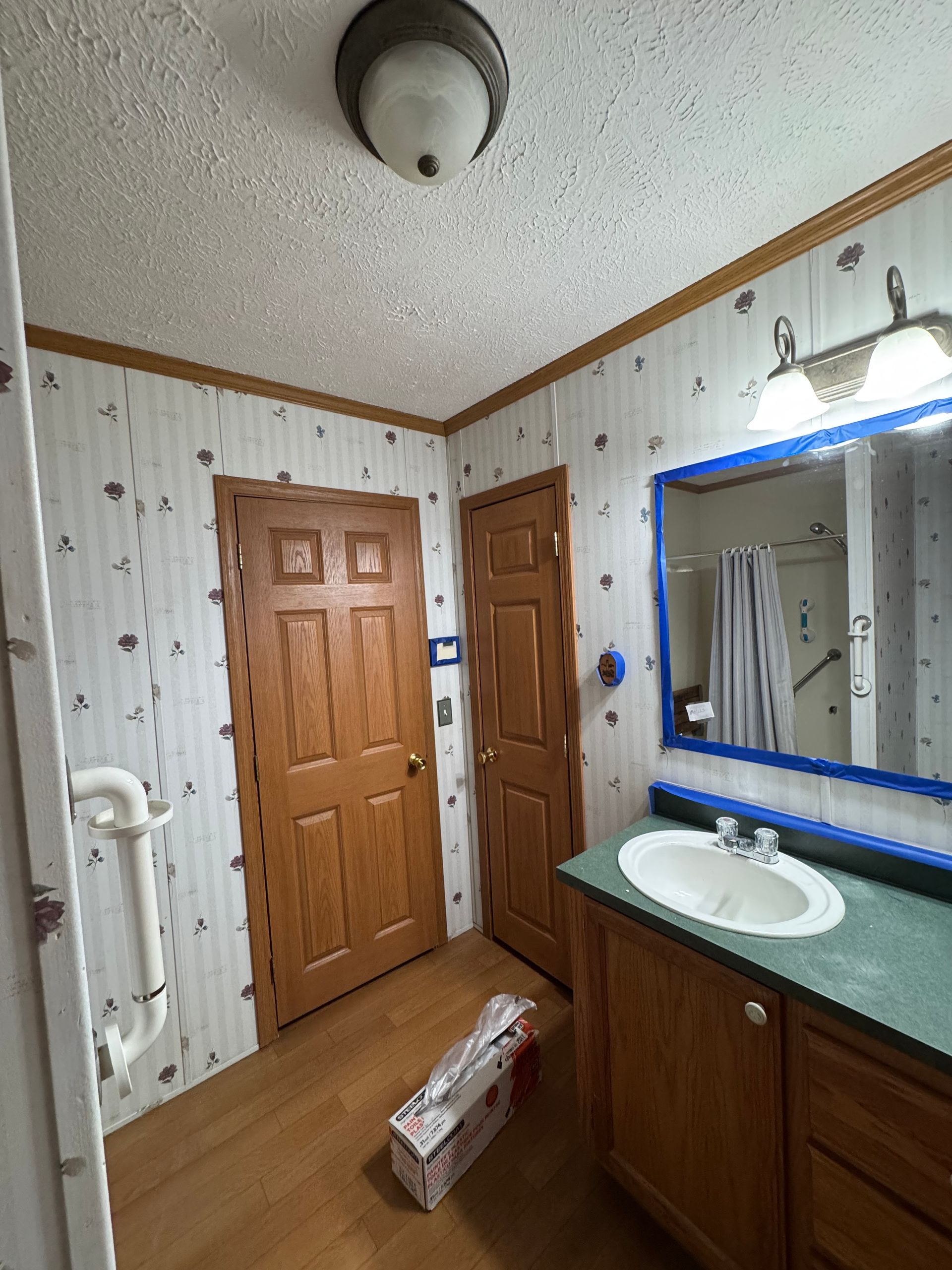 Bathroom with wooden doors, vanity sink, blue-framed mirror, and a box on the floor.