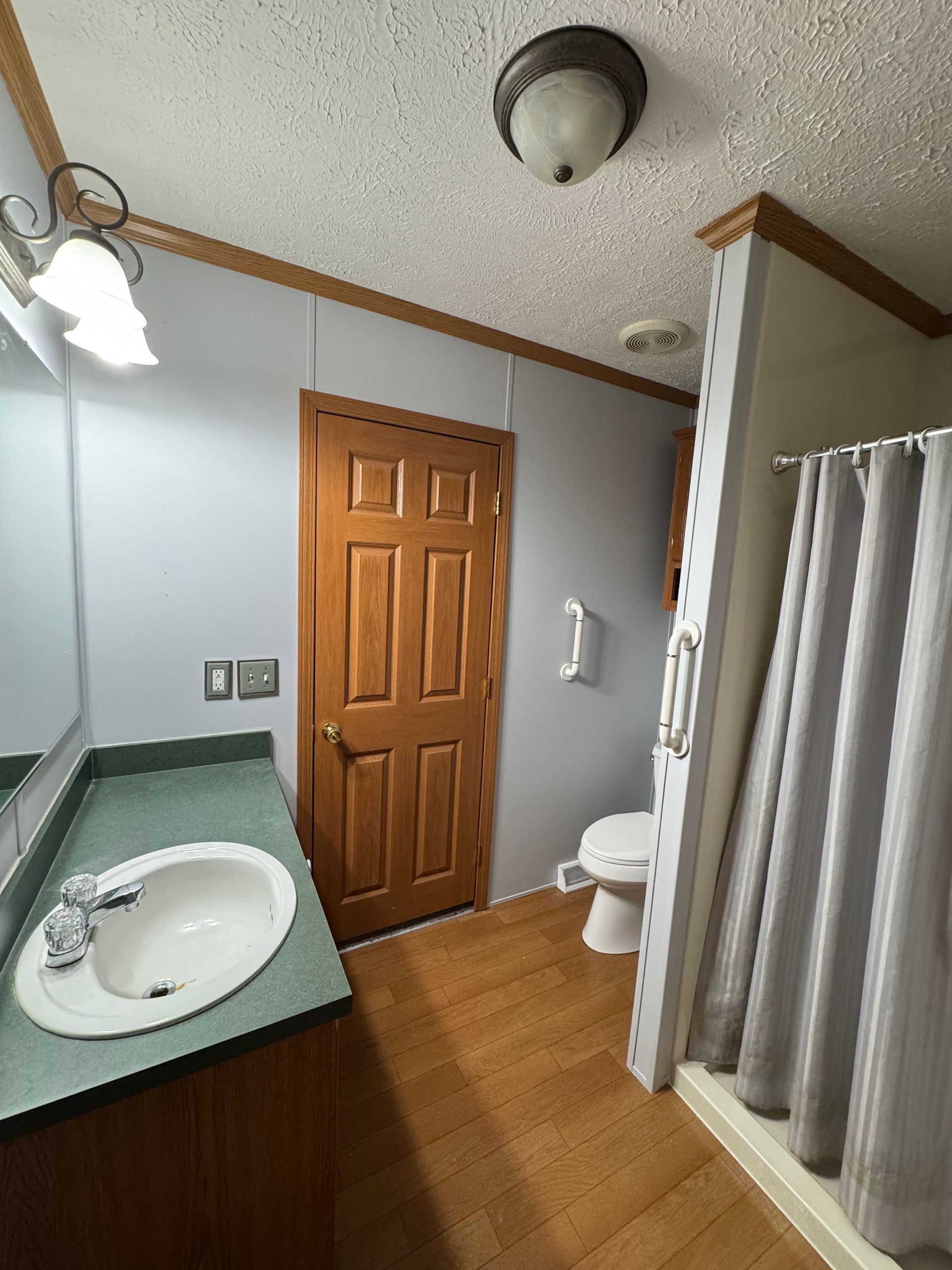 Small bathroom with sink, wooden door, toilet, and shower curtain.