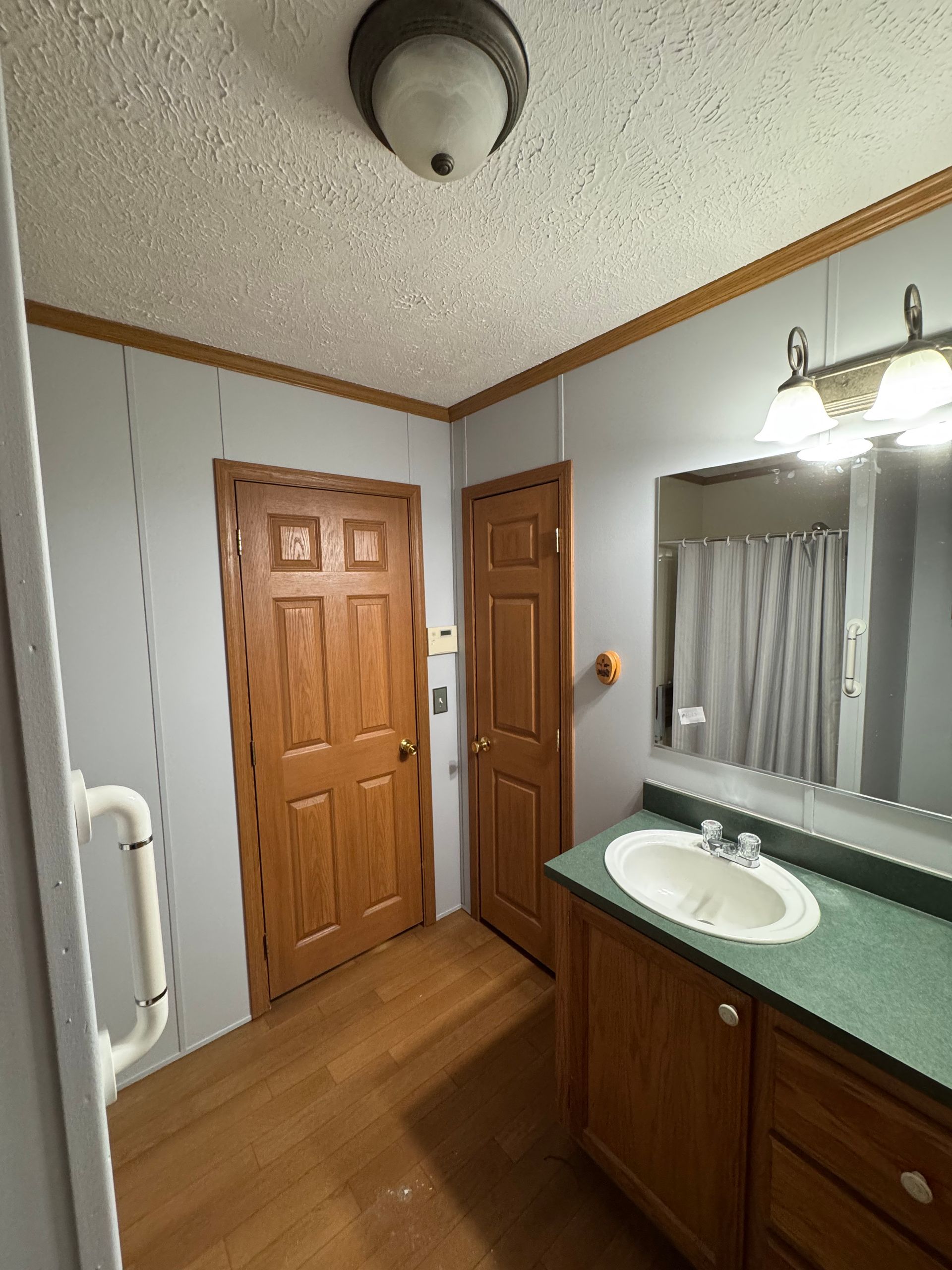 Bathroom vanity with mirror, wooden cabinets, sink, and two wood doors under a ceiling light.