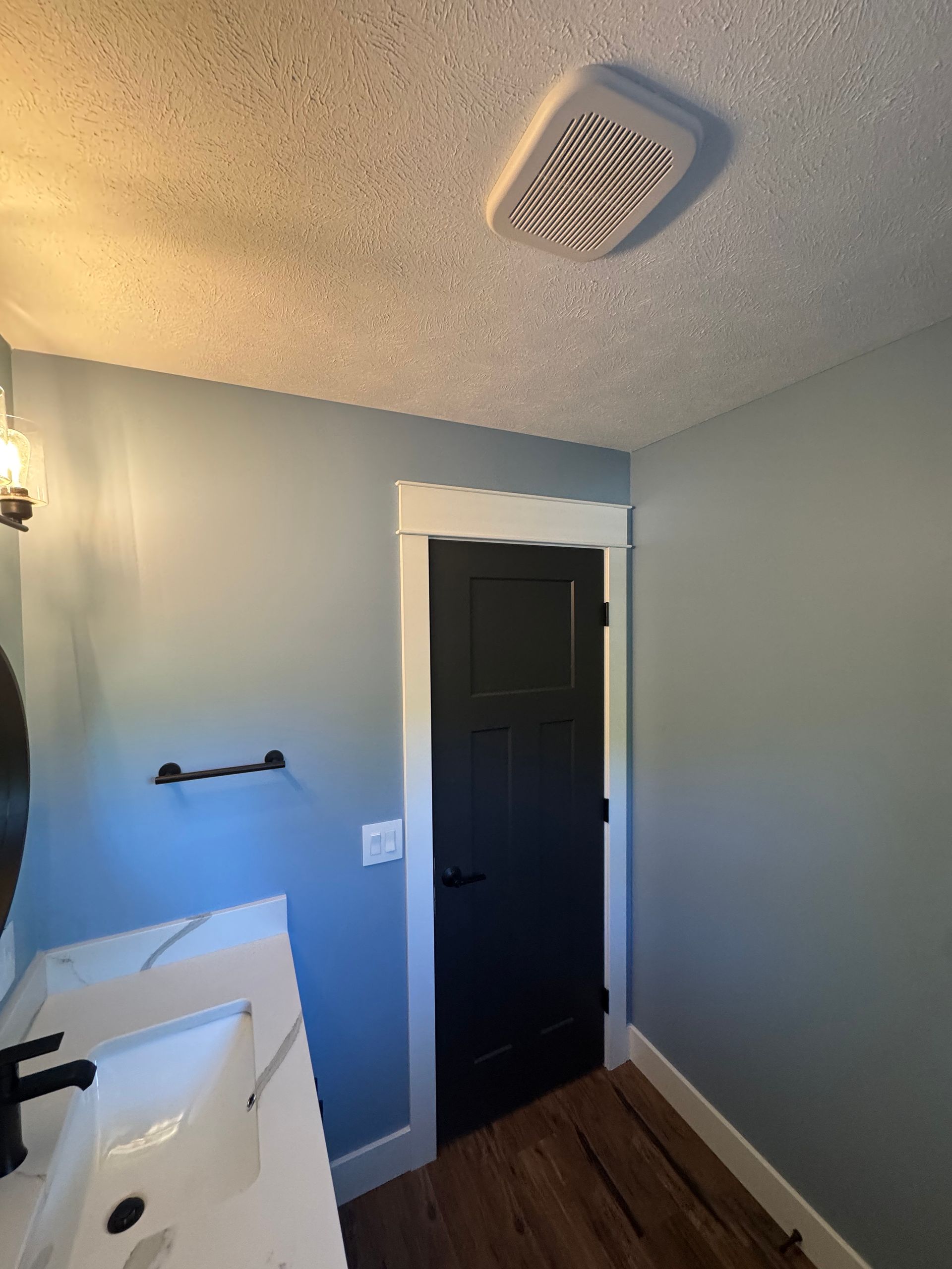 Small bathroom with a black door, white vanity, gray walls, and ceiling vent visible.