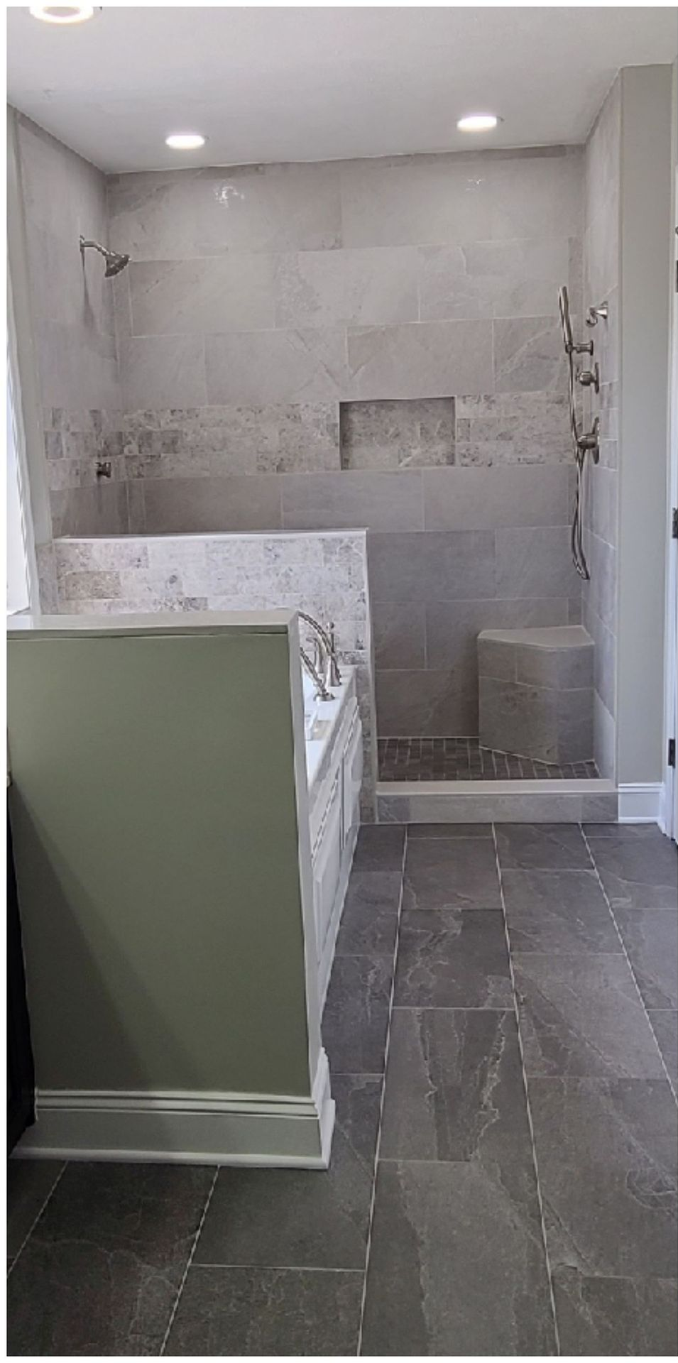 A bathroom with a large walk-in shower featuring a built-in bench, gray tile walls, and dark gray slate-style floor tiles.