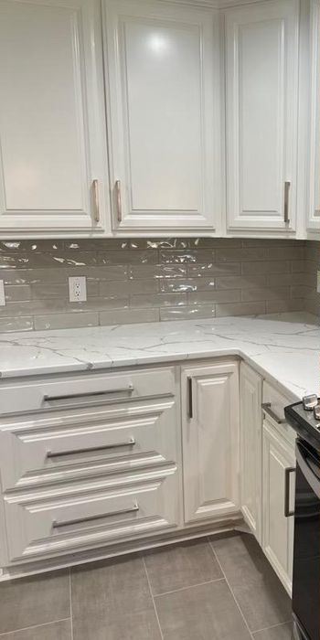 White cabinets with metallic handles, marble-patterned countertops, and a gray-tiled backsplash in a modern kitchen.