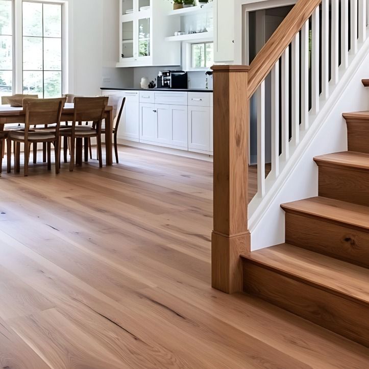 Interior view of a kitchen and dining area featuring light wood flooring, a wooden staircase, and white cabinets.
