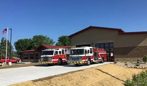 Fire station with two red-and-white fire trucks parked outside on a sunny day.