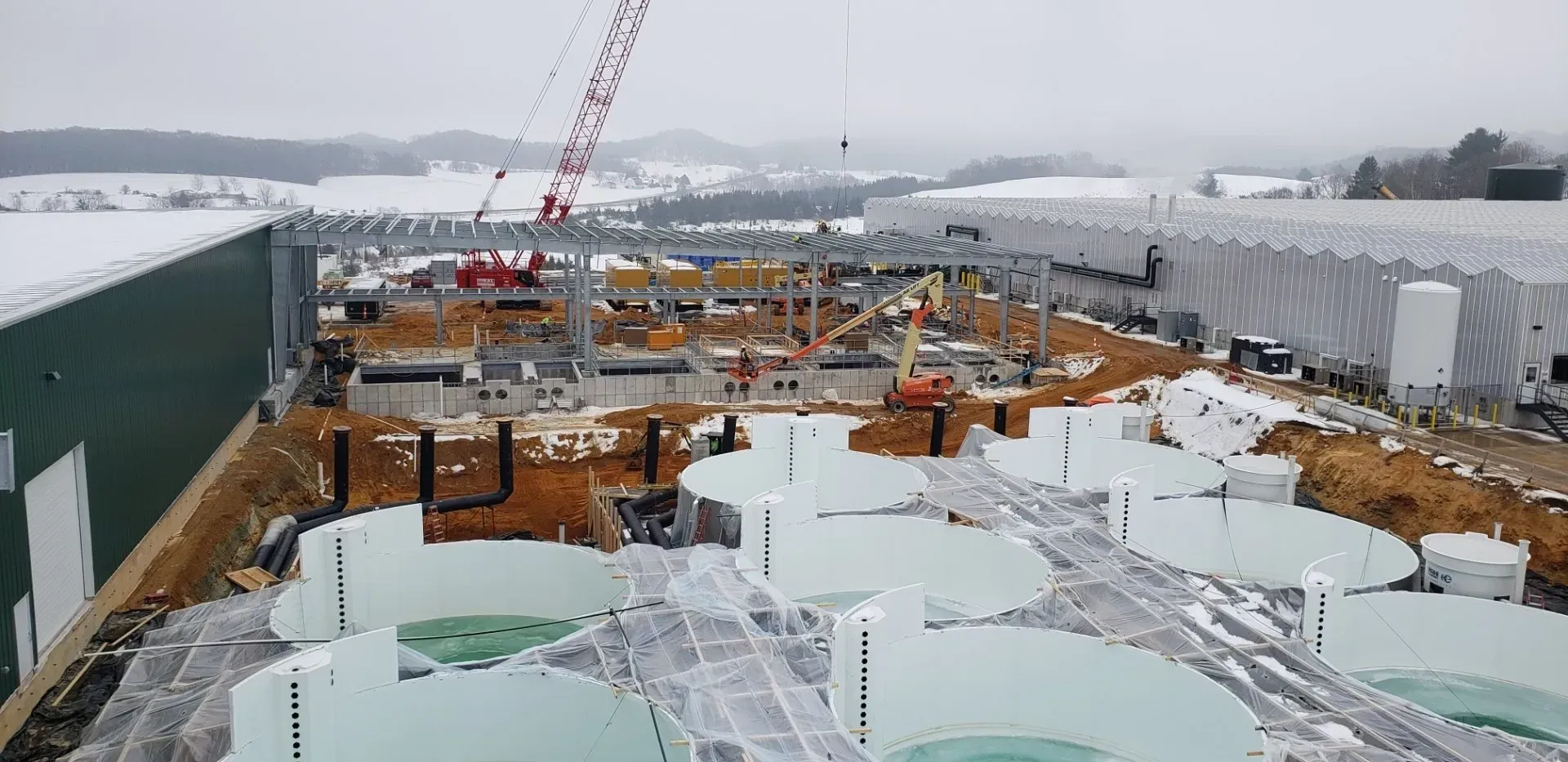 Snowy construction site with cranes and steel structures around large tanks