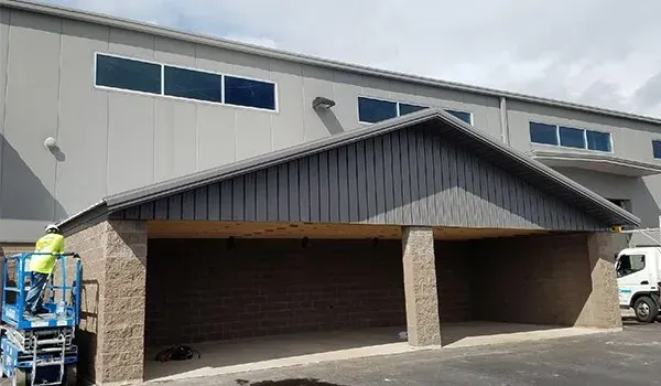 Two-car garage with brown doors and stone columns beneath a gray roof; worker on a lift at left