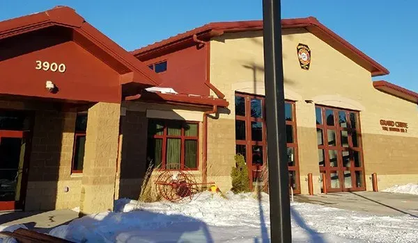 Snow-covered building with tan walls, red roof, and large glass doors in bright sunlight