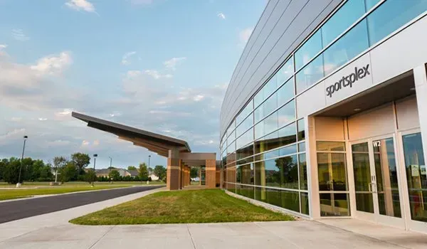 Modern glass office building with a curved facade and landscaped entrance under a partly cloudy sky