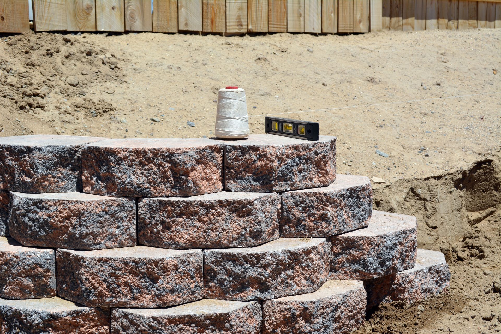 Stone retaining wall under construction with stacked blocks, sand, and a bucket on top