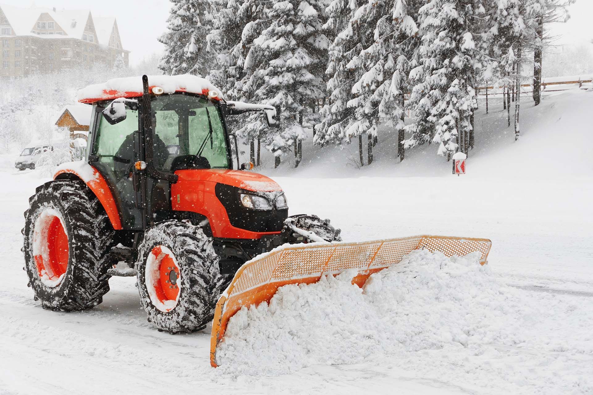 Orange tractor clearing snow on a snowy road beside snow-covered trees Orange tractor clearing snow on a snowy road beside snow-covered trees