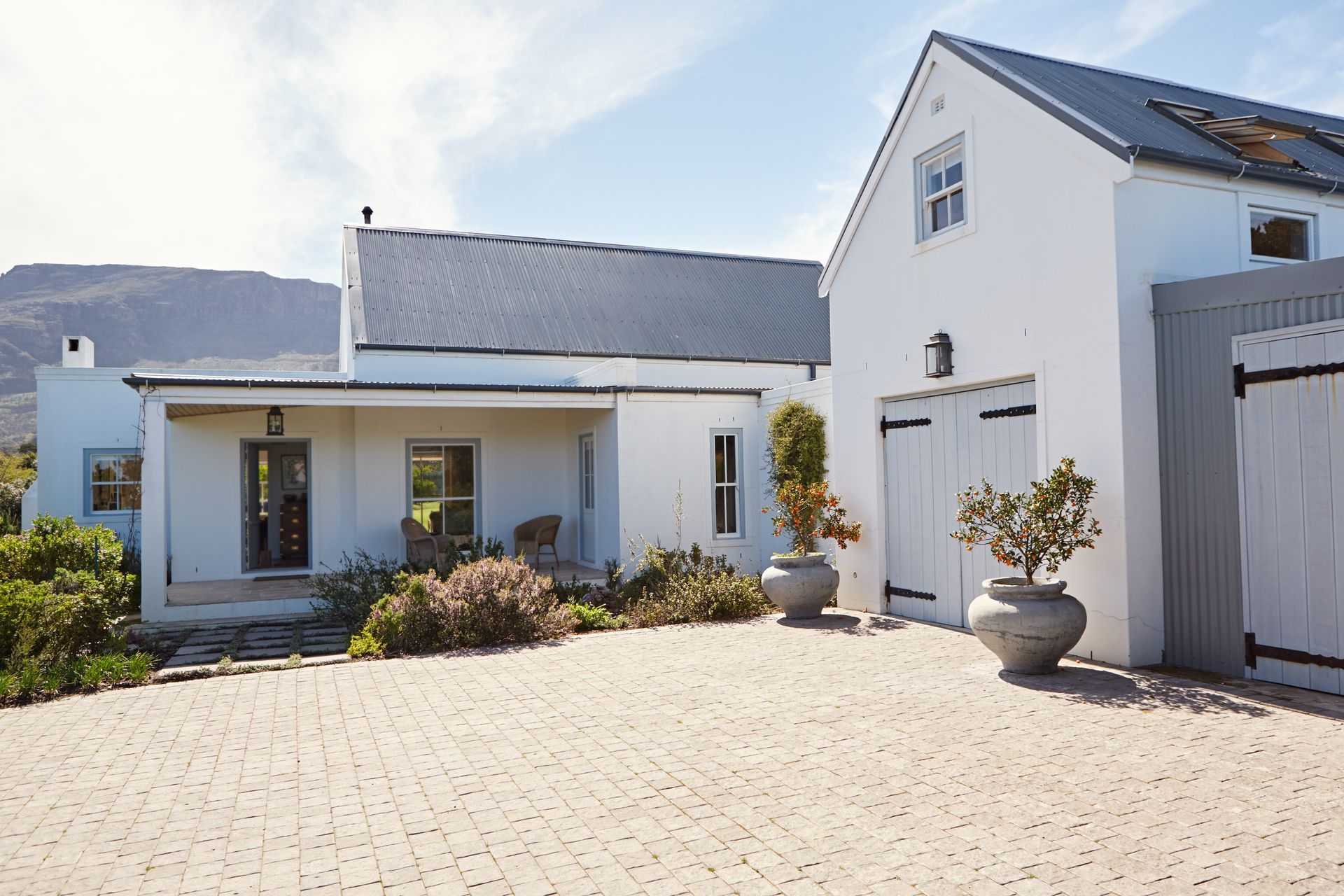 White modern house with a gray roof, front porch, and large paved driveway under bright sunlight