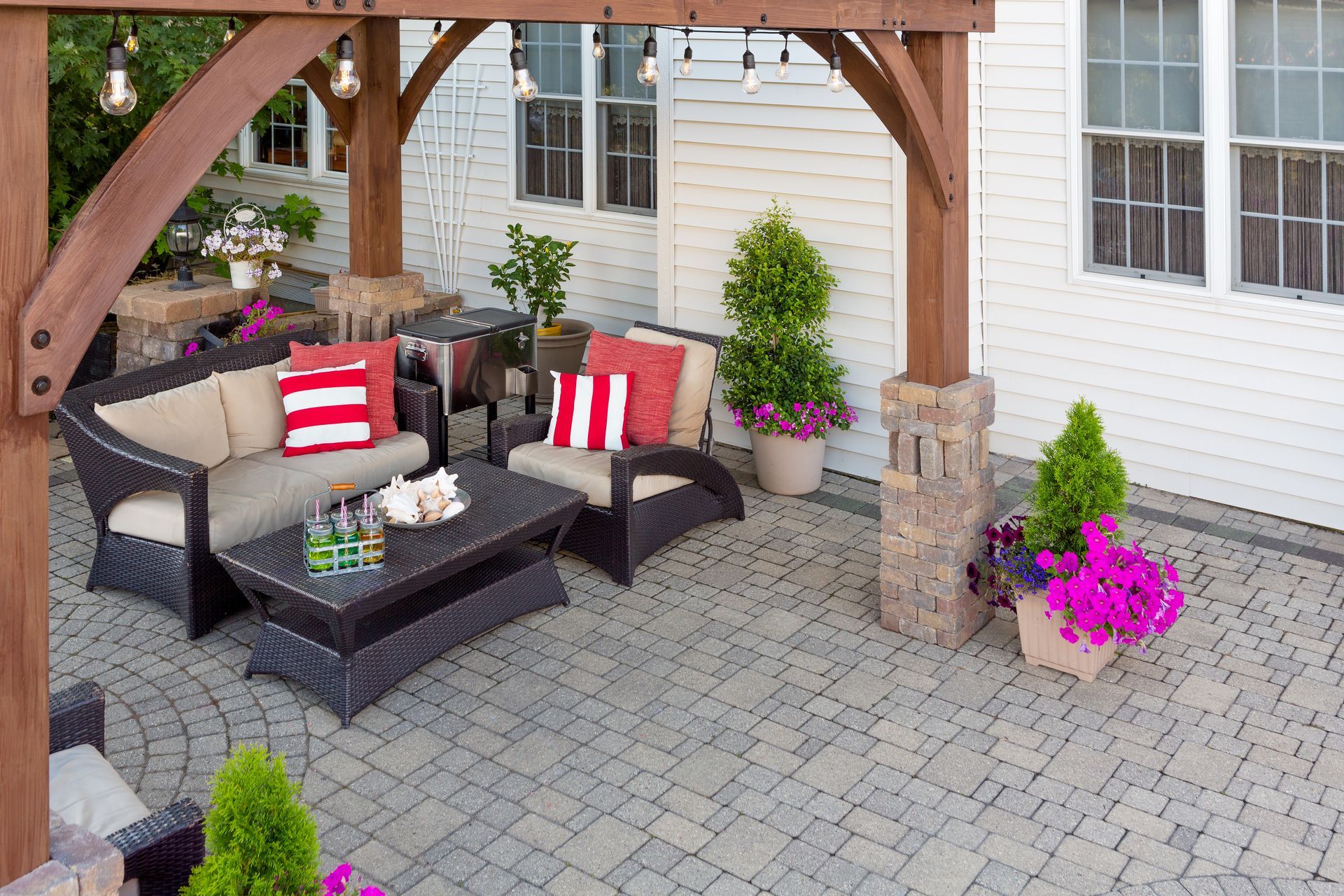 Covered patio with wicker seating, striped cushions, coffee table, and potted flowers on a stone paver patio Covered patio with wicker seating, striped cushions, coffee table, and potted flowers on a stone paver patio