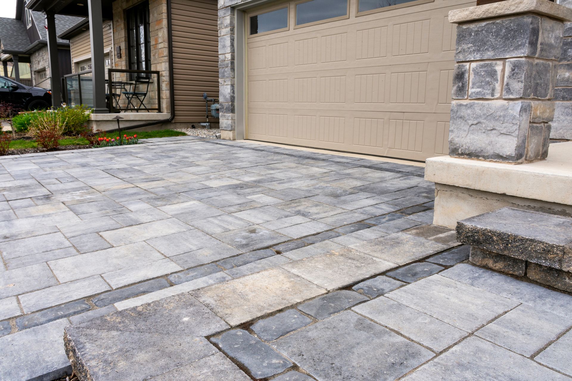 Stone paver driveway leading to a beige garage beside a house entrance