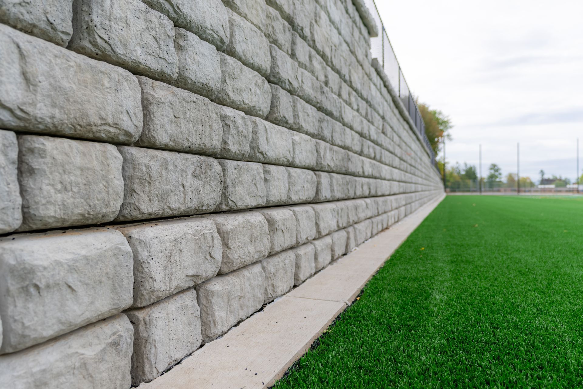 Long stone retaining wall beside a bright green lawn under an overcast sky