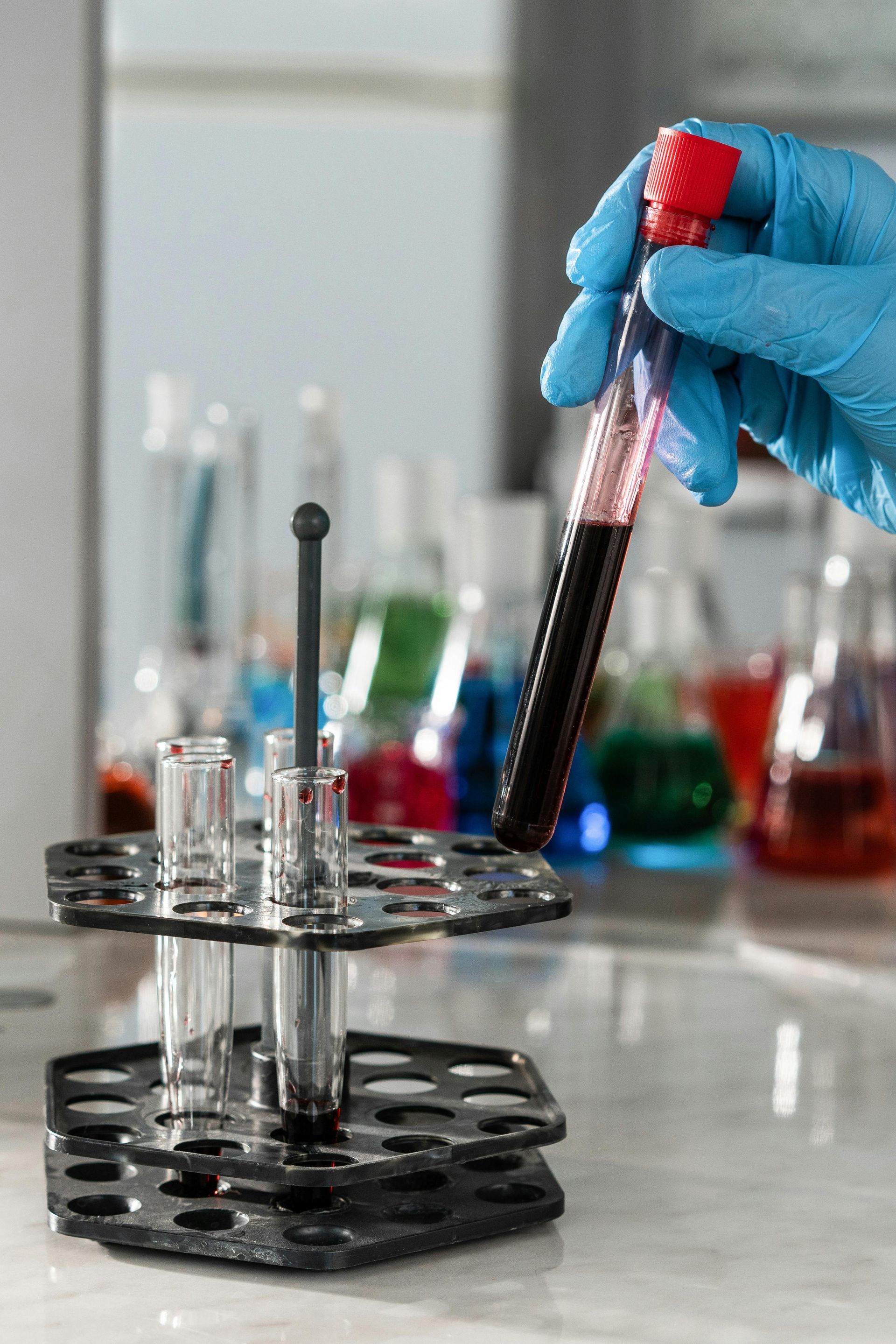 Gloved hand holding a test tube over a lab rack with colored liquids in the background