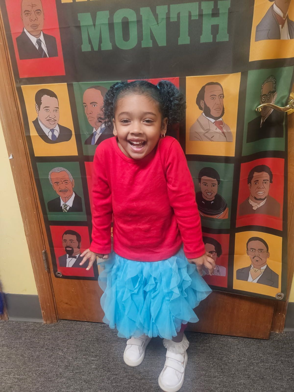 A little girl stands in front of a black history month poster