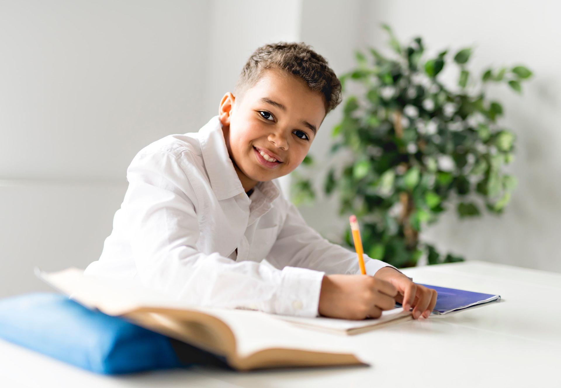 A young boy is sitting at a table writing in a notebook.
