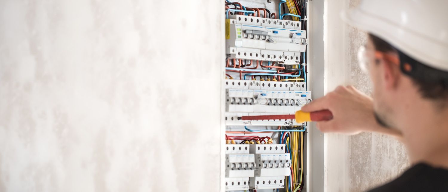 An electrician is working on an electrical box with a screwdriver.