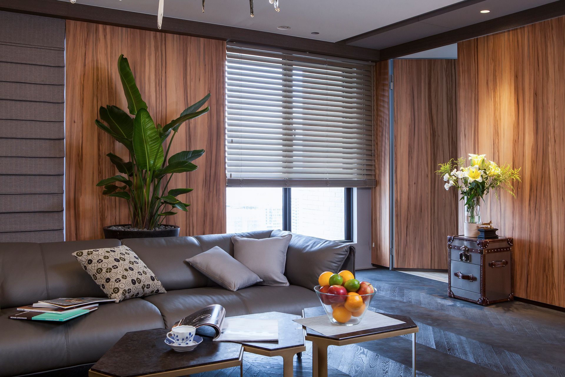 Living room with brown leather sofa, wood panel walls, window with blinds, and indoor plants.