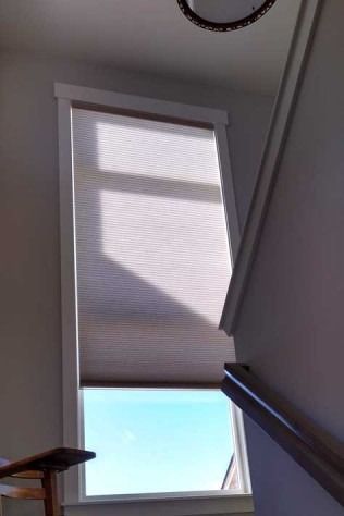 Window with a light beige shade, blue sky visible, and a staircase railing.