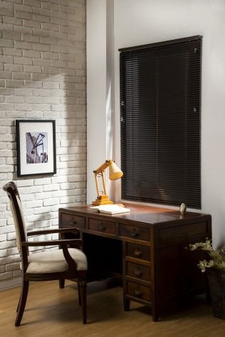 Desk with chair, lamp, and window with dark blinds against brick wall.